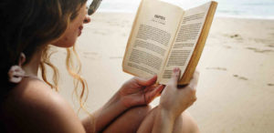 Frau liest Buch über Geld, Finanzen, Cashflow und finanzielle Freiheit, am Strand